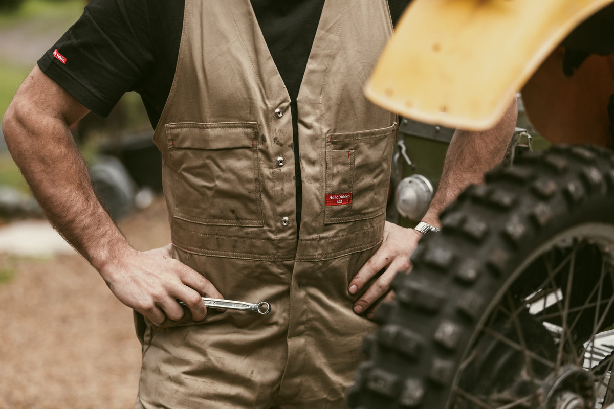 Hard Yakka khaki work overalls, worker holding a spanner beside a dirt bike